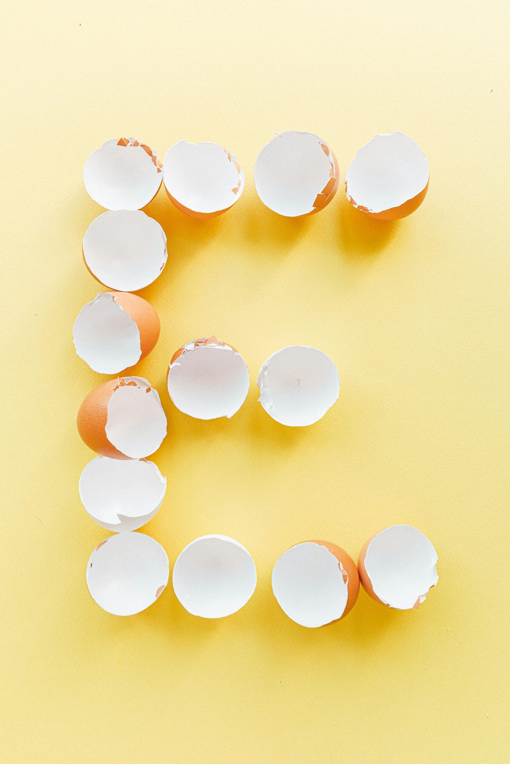Artistic display of eggshells forming a letter E on a bright yellow backdrop.