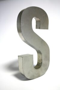 Close-up of a metallic letter S sculpture made of silver iron on a white background.