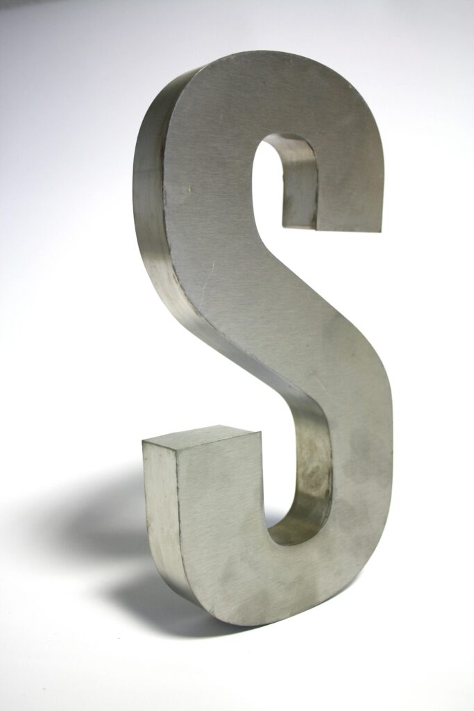 Close-up of a metallic letter S sculpture made of silver iron on a white background.