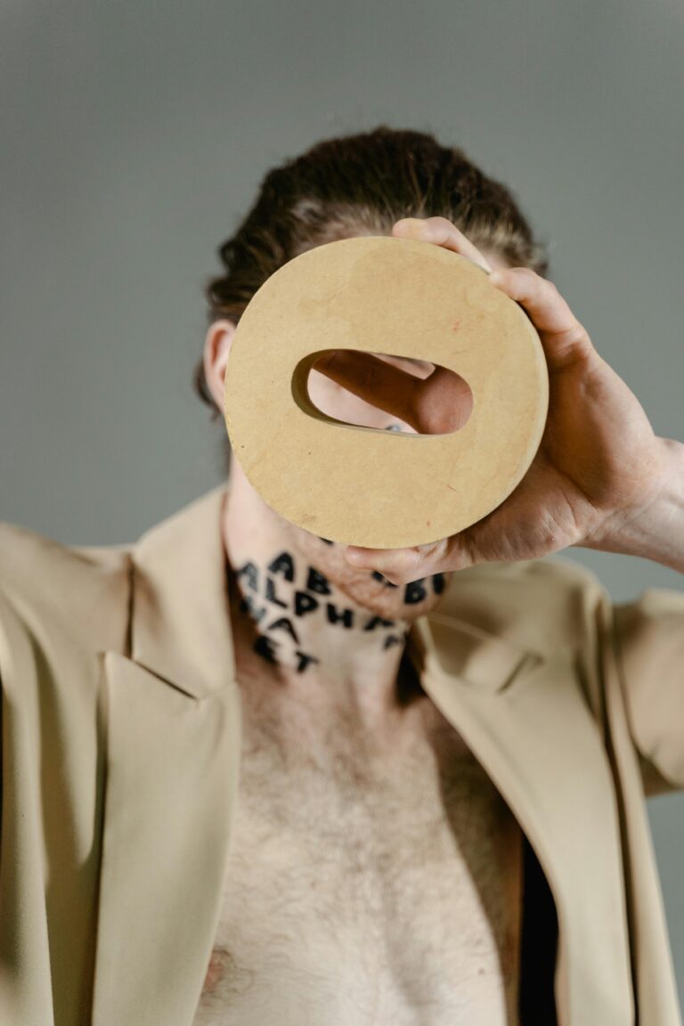 Artistic portrait featuring a man with a beige coat holding a letter block over his face.